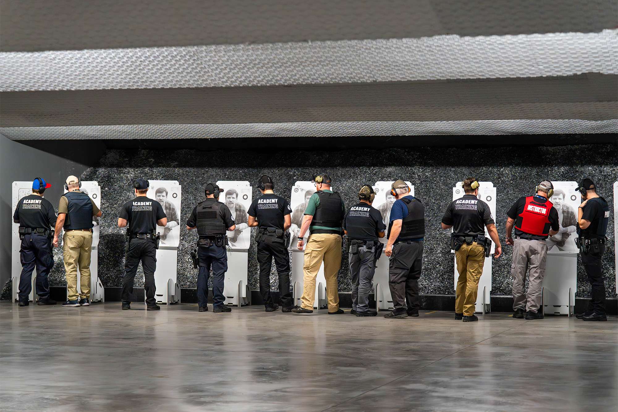 Police academy trainees and instructors inspect targets at a shooting range during a firearms training session.