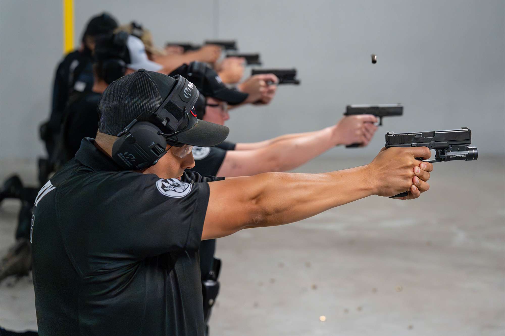 Police academy trainees in uniform fire handguns at a shooting range during a firearms training session.