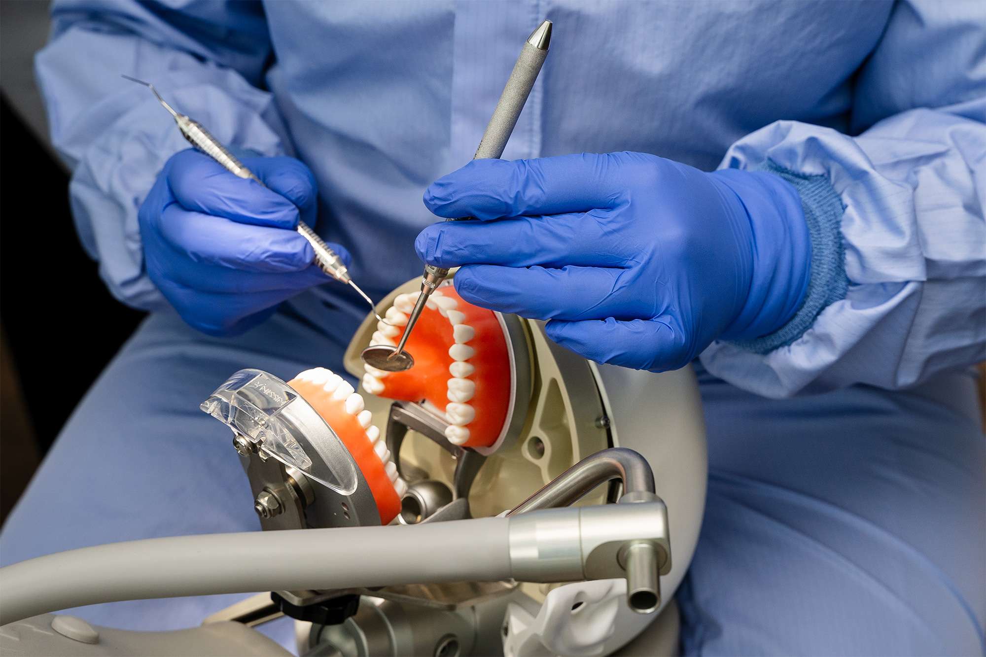 Dental professional with blue gloves working on dental molds with tools and mirror, demonstrating Prosthodontic procedures.