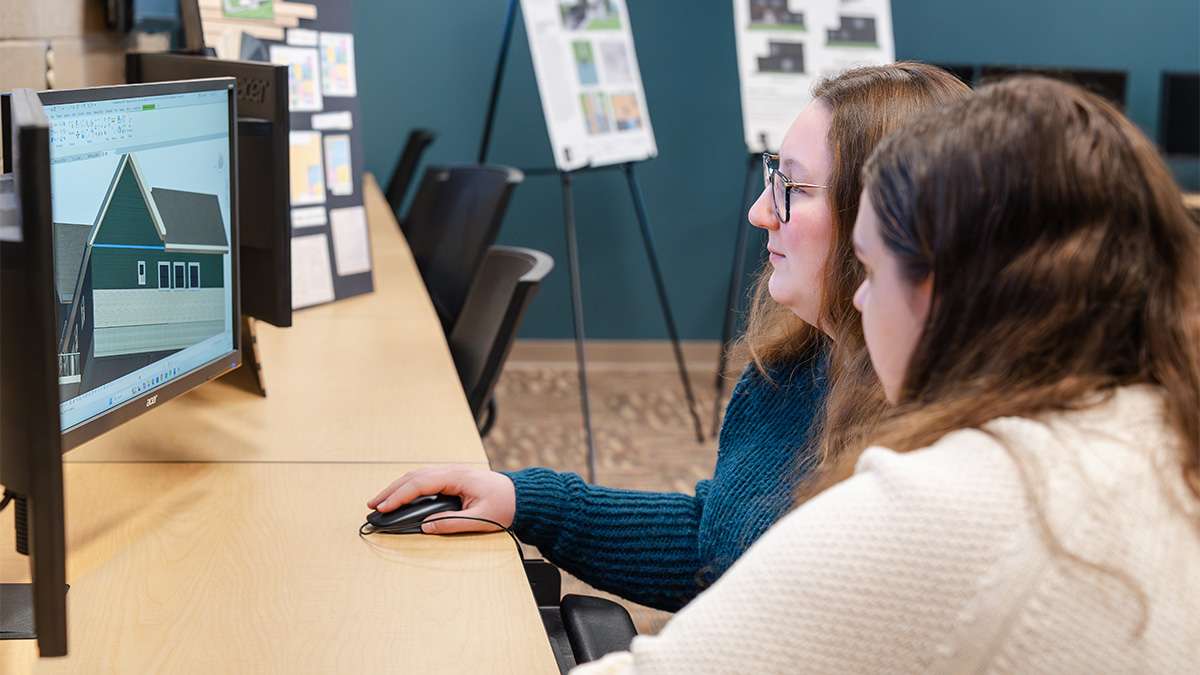 Students collaborate on architectural 3D house design using computer in classroom setting.