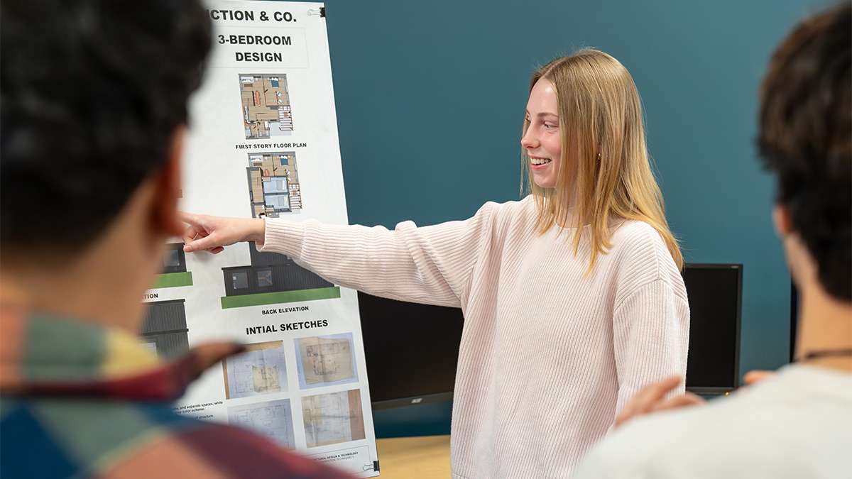Student presenting 3-bedroom home design floor plans and sketches to attentive classmates.