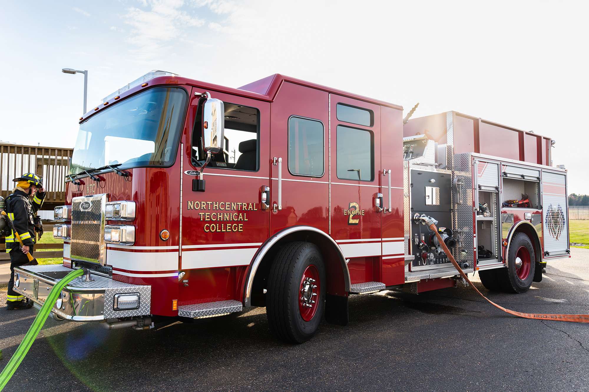 Fire engine labeled Northcentral Technical College parked as firefighters handle hoses during training.