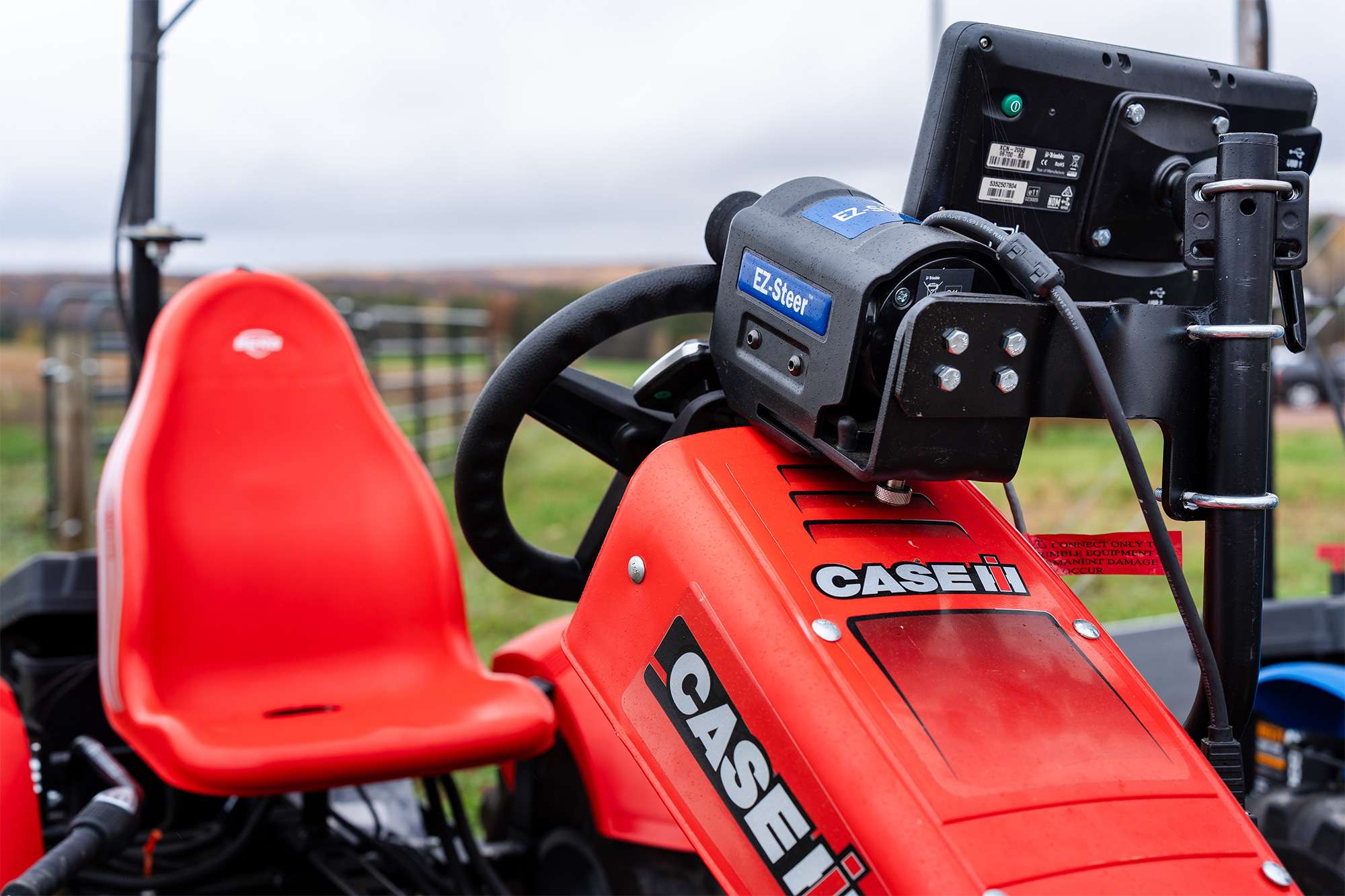 Close-up of red CASE IH tractor cockpit showing steering wheel, control panel with digital display, joystick, and seat.