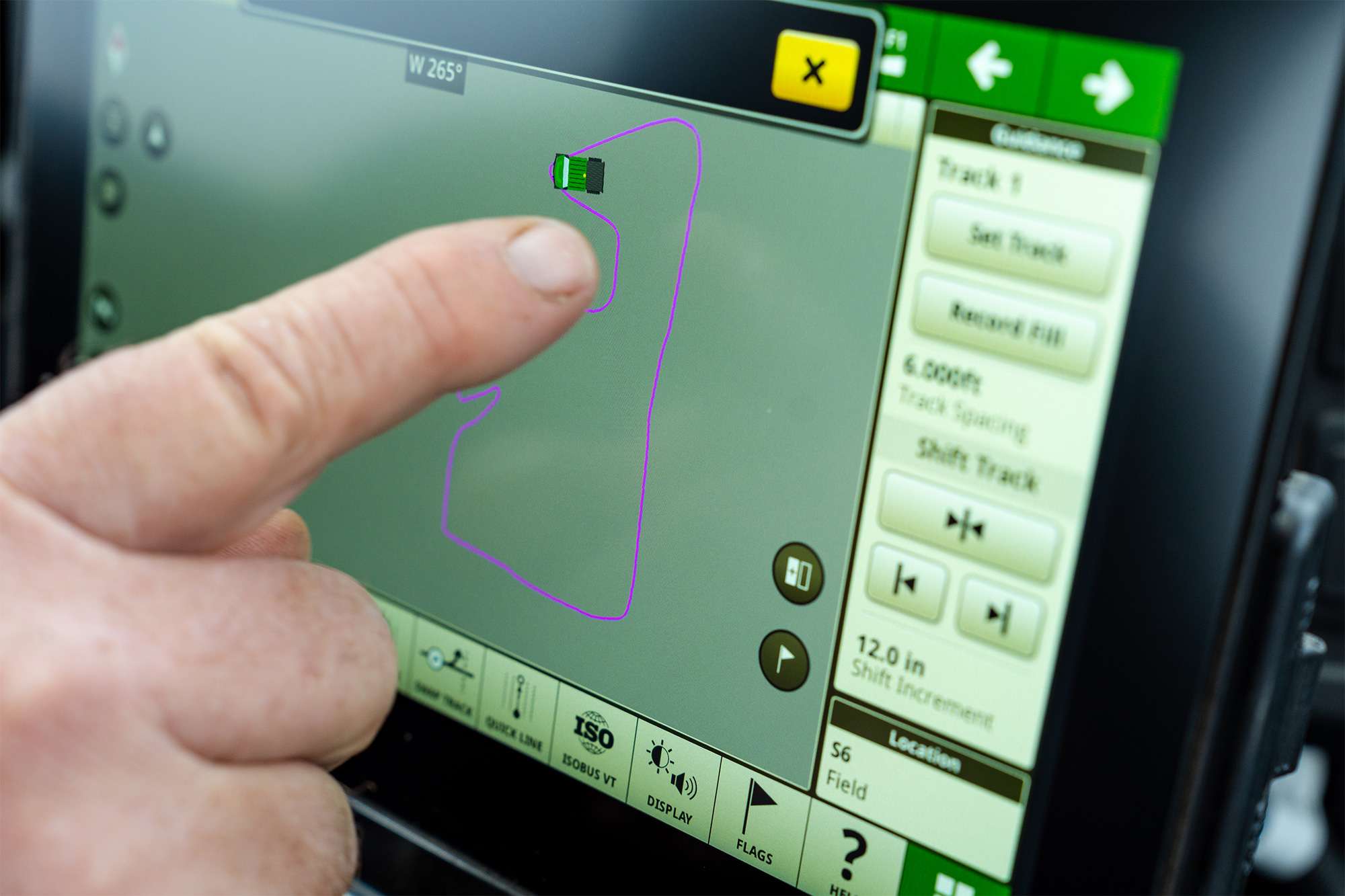 Left index finger tapping a touchscreen navigation panel displaying a green interface, purple field outline.