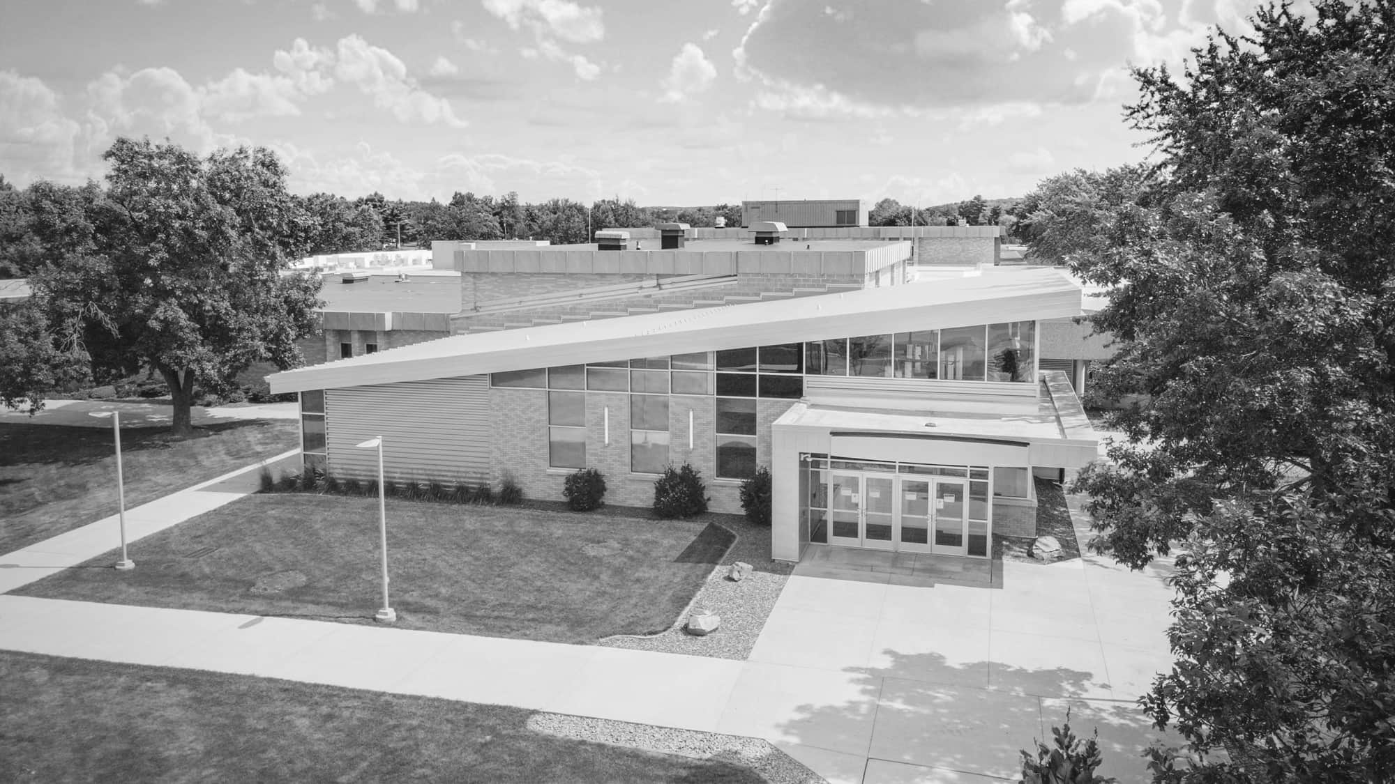 An aerial view of NTC's Wausau Campus main entrance on a sunny summer day. Trees and greenery frame the spacious side walks that lead up to the light-brown brick building.